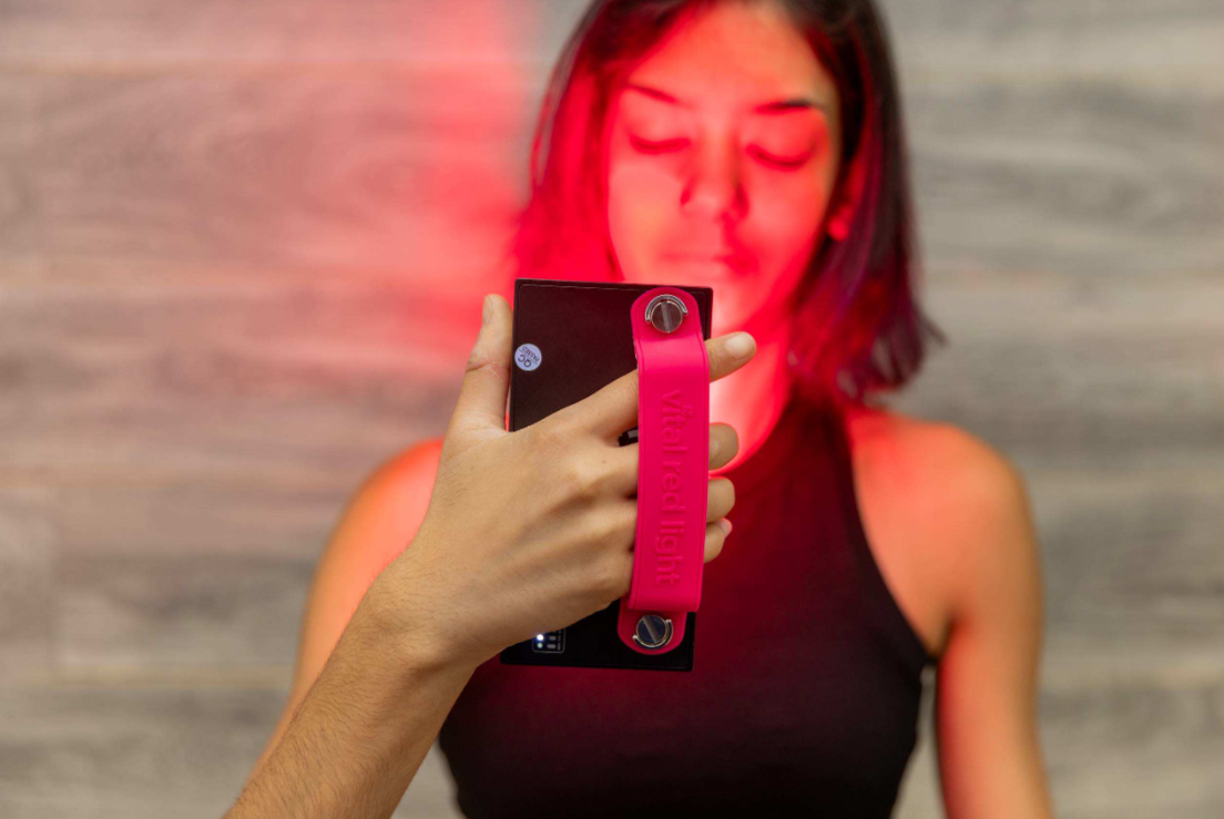 Woman using a Vital red light therapy handheld device on her face