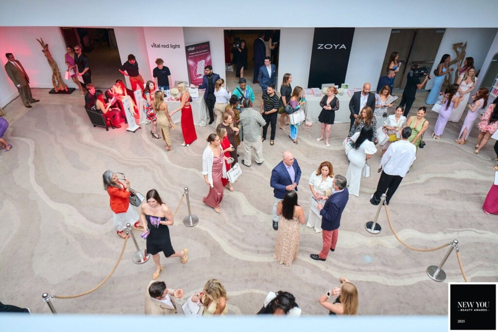 A group of people socializing at the New You Awards event, where some attendees are seated while others stand and engage in conversation. Various banners are displayed on the walls around the room, celebrating achievements.